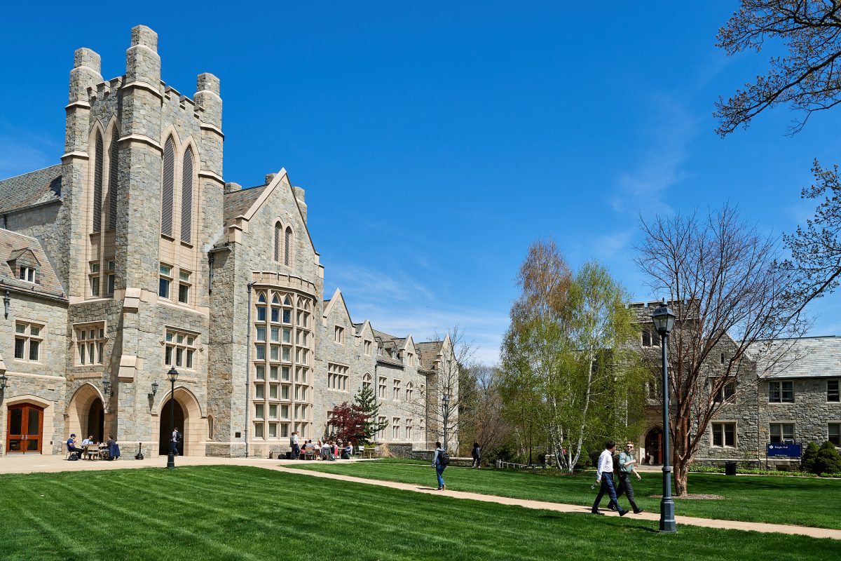 A view of the Meskill Law Library at the UConn Law campus in Hartford with students sitting at tables on a patio and walking down pathways in the foreground